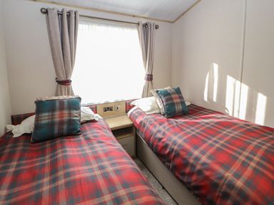 A bedroom with two single beds with plaid bedspreads and pillows and a window with curtains at Gressingham 7 in Warton near Carnforth