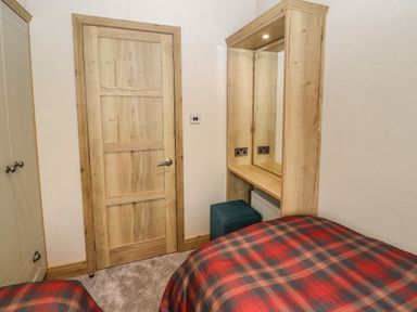 A bedroom with a wooden door a wardrobe a vanity mirror with lights and a stool two beds with plaid bedspreads at Gressingham 7 Warton near Carnforth