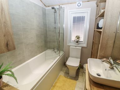 A bathroom with a bathtub shower toilet sink and wooden shelves at Gressingham 7 in Warton near Carnforth