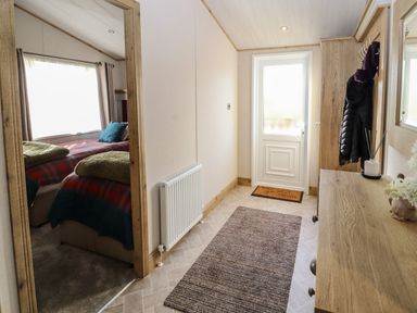 An entrance hallway with a small wooden table coat rack and a door leading outside with a bedroom visible through an open door at Gressingham 7 in Warton near Carnforth