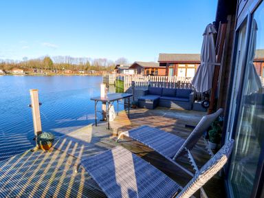 A wooden deck with lounge chairs and a sofa overlooking a lake at Gressingham 7 in Warton near Carnforth