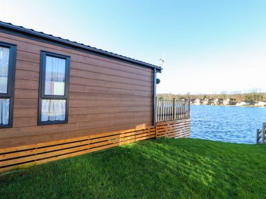 Side view of a wooden cabin with windows on grass by the water at Gressingham 7 in Warton near Carnforth