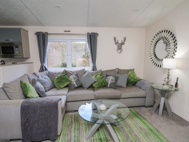 A living room with a sectional sofa with green and gray cushions and two glass tables at 43 The Deri in Llanarth