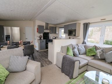 A living room with sofas and cushions next to a kitchen and dining table with chairs at 43 The Deri in Llanarth