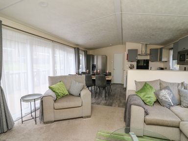 An open plan living room and kitchen with sofas dining table and kitchen appliances at 43 The Deri in Llanarth