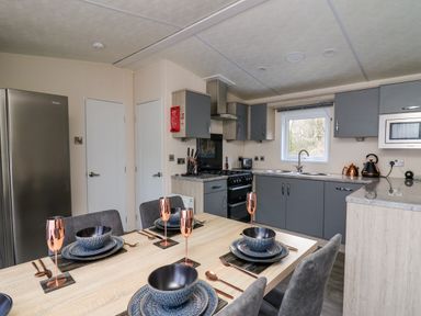 A kitchen with grey cabinets a dining table set with blue dishes and copper utensils at 43 The Deri in Llanarth