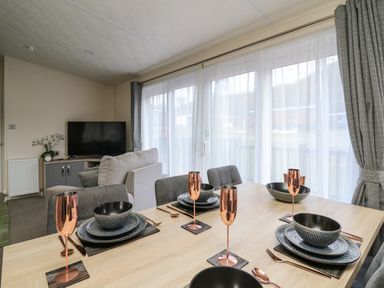 A dining table set with black dishes and copper glasses in a room with a sofa and a TV at 43 The Deri in Llanarth