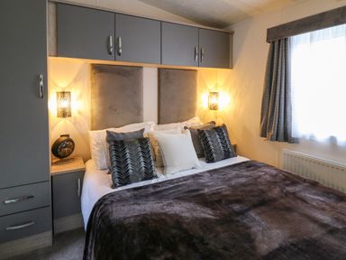 A bedroom with a bed pillows and a blanket with built in cabinets and a window at 43 The Deri in Llanarth