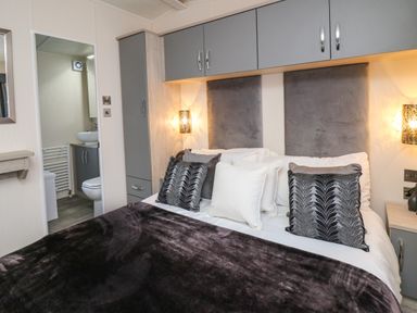 A bedroom with a bed with pillows and a blanket and a bathroom visible through an open door at 43 The Deri in Llanarth