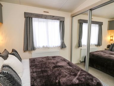 A bedroom with a bed near a window and mirrored sliding closet doors at 43 The Deri in Llanarth