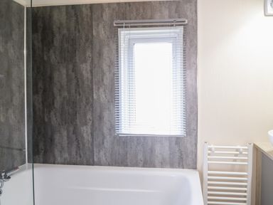 A bathroom with a bathtub a window with blinds and a towel radiator at 43 The Deri in Llanarth