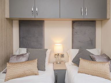 A bedroom with two single beds a bedside table with a lamp and overhead cabinets at 43 The Deri in Llanarth