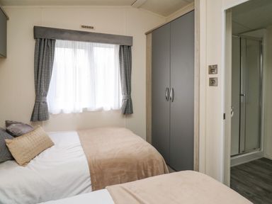 A bedroom with two beds gray curtains a wardrobe and a door leading to a shower at 43 The Deri in Llanarth