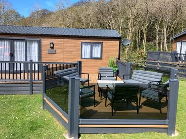 A patio area with outdoor seating and table next to a wooden cabin surrounded by trees at 43 The Deri in Llanarth