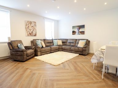 A living room with a large sectional sofa and recliner chairs a white rug and two animal paintings at Gwydyr Bach 1 in Llanrwst