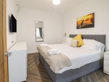 A bedroom with a bed with pillows and folded towels a dresser with a TV on the wall and a mirror on the wall at Gwydyr Bach 1 in Llanrwst
