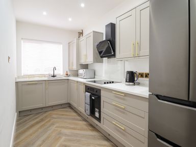 A kitchen with grey cabinets and gold handles a black oven a microwave a kettle a window and a stainless steel fridge at Gwydyr Bach 1 in Llanrwst