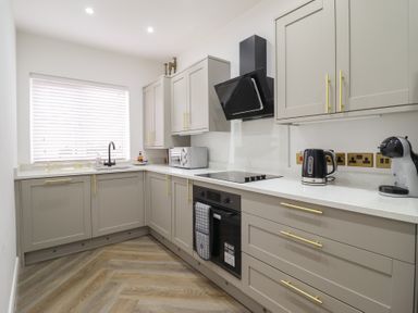 A kitchen with grey cabinets a black oven a stove a microwave a kettle and a coffee machine at Gwydyr Bach 1 Llanrwst