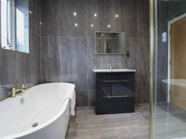 A bathroom with a freestanding bathtub a vanity unit with sink and mirror and a glass shower enclosure at Gwydyr Bach 1 in Llanrwst