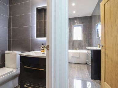 A bathroom with a toilet sink and mirror on one side and a bathtub sink and window on the other side at Gwydyr Bach 1 in Llanrwst