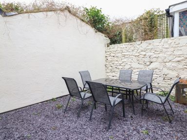 An outdoor patio area with a glass table and six chairs on a gravel surface at Gwydyr Bach 1 in Llanrwst