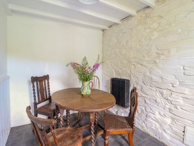 A dining area with a round wooden table and four wooden chairs a vase with flowers on the table a white textured wall and a black radiator in Nyth Yr Eryr Blaenau Ffestiniog