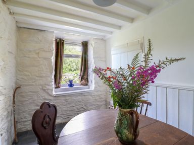 A dining area with a wooden table and chairs a vase with flowers on the table and a window with curtains at Nyth Yr Eryr in Blaenau Ffestiniog