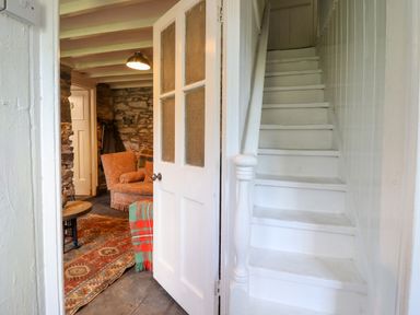 A hallway with white stairs and an open door showing a room with a patterned rug and an orange armchair at Nyth Yr Eryr in Blaenau Ffestiniog