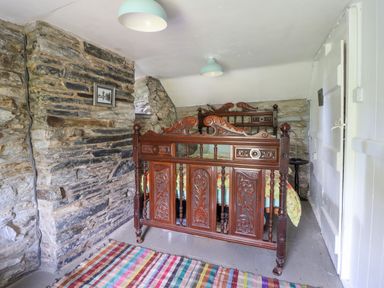 A bedroom with two wooden carved beds stone walls and a colorful striped rug on the floor at Nyth Yr Eryr in Blaenau Ffestiniog