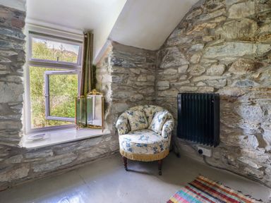 A stone wall corner with a floral armchair near an open window and a black wall heater at Nyth Yr Eryr in Blaenau Ffestiniog