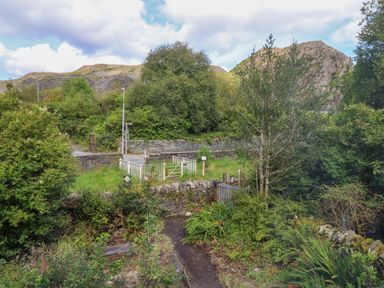 A garden path leading to a gate with a stone wall and trees around at Nyth Yr Eryr in Blaenau Ffestiniog
