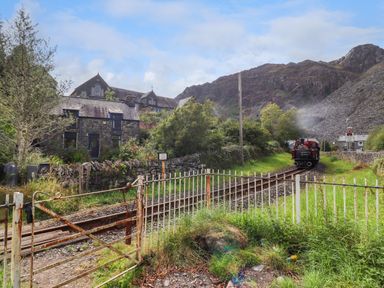A rural train track with a small steam locomotive near stone buildings and hills at Nyth Yr Eryr in Blaenau Ffestiniog