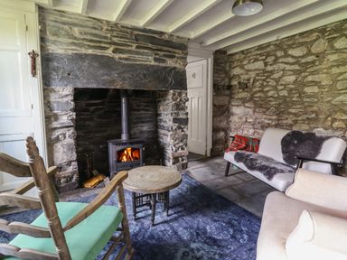 A room with stone walls a wood burning stove two armchairs a small wooden table and a couch with a fur throw at Nyth Yr Eryr in Blaenau Ffestiniog