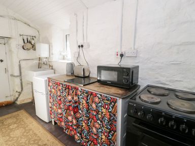 A kitchen with a small fridge a sink a toaster kettle microwave and stove with a floral curtain below the counter at Nyth Yr Eryr in Blaenau Ffestiniog
