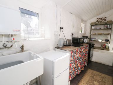 A kitchen with a white sink fridge toaster kettle microwave and shelves with dishes at Nyth Yr Eryr in Blaenau Ffestiniog
