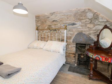 A bedroom with a metal bed and floral bedding beside a stone wall and a wooden dressing table with a round mirror at Nyth Yr Eryr in Blaenau Ffestiniog