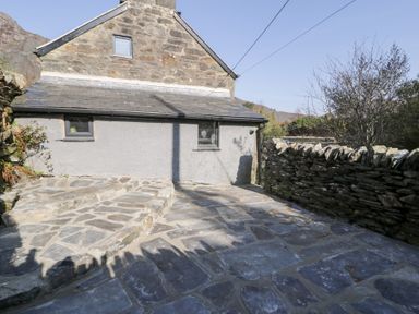 An outdoor stone patio with steps next to a stone wall and a stone building at Nyth Yr Eryr in Blaenau Ffestiniog