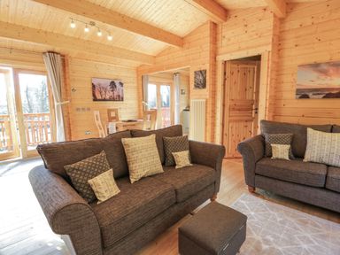A living room with two brown sofas and a small ottoman next to a dining table in a wooden cabin at Little Lodge in Balminnoch near Glenluce