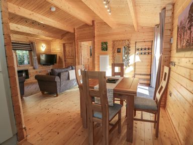 A wooden interior dining area with a table and chairs and a living area with sofas and a wall mounted television at Little Lodge in Balminnoch near Glenluce