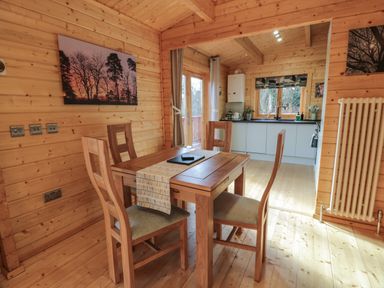 A dining area with wooden table and four chairs next to a kitchen in a wooden interior at Little Lodge Balminnoch near Glenluce