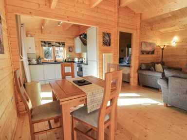 A wooden dining table with four chairs next to a kitchen and a living area with sofas at Little Lodge in Balminnoch near Glenluce