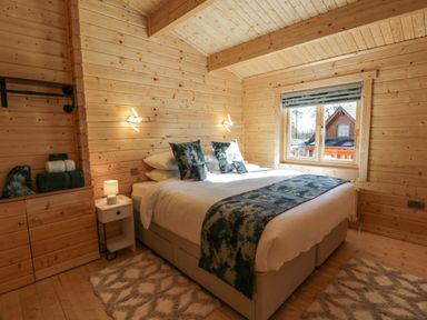 A bedroom with a double bed two wall lights and a window in a wooden cabin at Little Lodge in Balminnoch near Glenluce