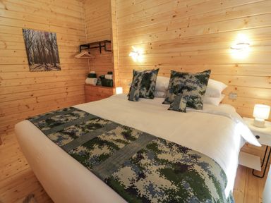 A bedroom with a double bed with patterned pillows and throw in a wooden cabin at Little Lodge in Balminnoch near Glenluce