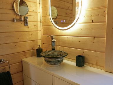 A bathroom with wooden walls a patterned sink an illuminated round mirror and a towel at Little Lodge Balminnoch near Glenluce