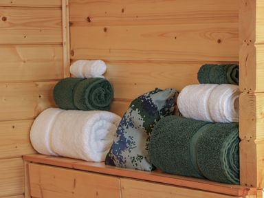 Rolled white and green towels on a wooden shelf with a camouflage bag at Little Lodge Balminnoch near Glenluce