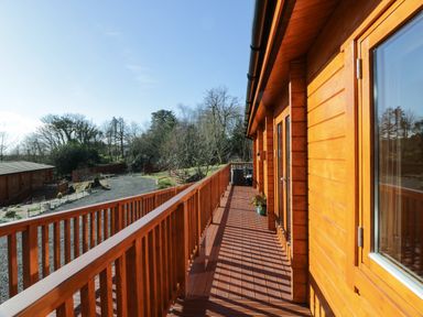 A wooden balcony attached to a wooden house overlooking a garden area with trees and gravel at Little Lodge in Balminnoch near Glenluce