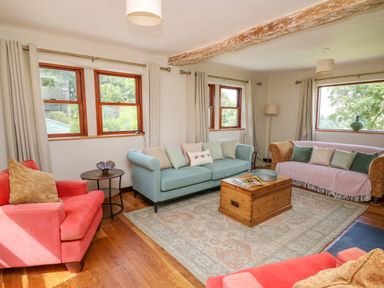 A living room with two coral armchairs a blue sofa a patterned sofa and a wooden coffee table at Oak Apple Cottage in Presteigne