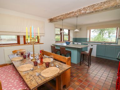 A kitchen and dining area with a wooden table set for dining and a kitchen island with stools at Oak Apple Cottage in Presteigne