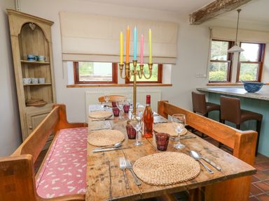 A dining area with a wooden table set with placemats glassware cutlery and a candelabra with colorful candles at Oak Apple Cottage in Presteigne