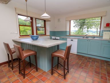 A kitchen with a central island and three brown chairs at Oak Apple Cottage in Presteigne